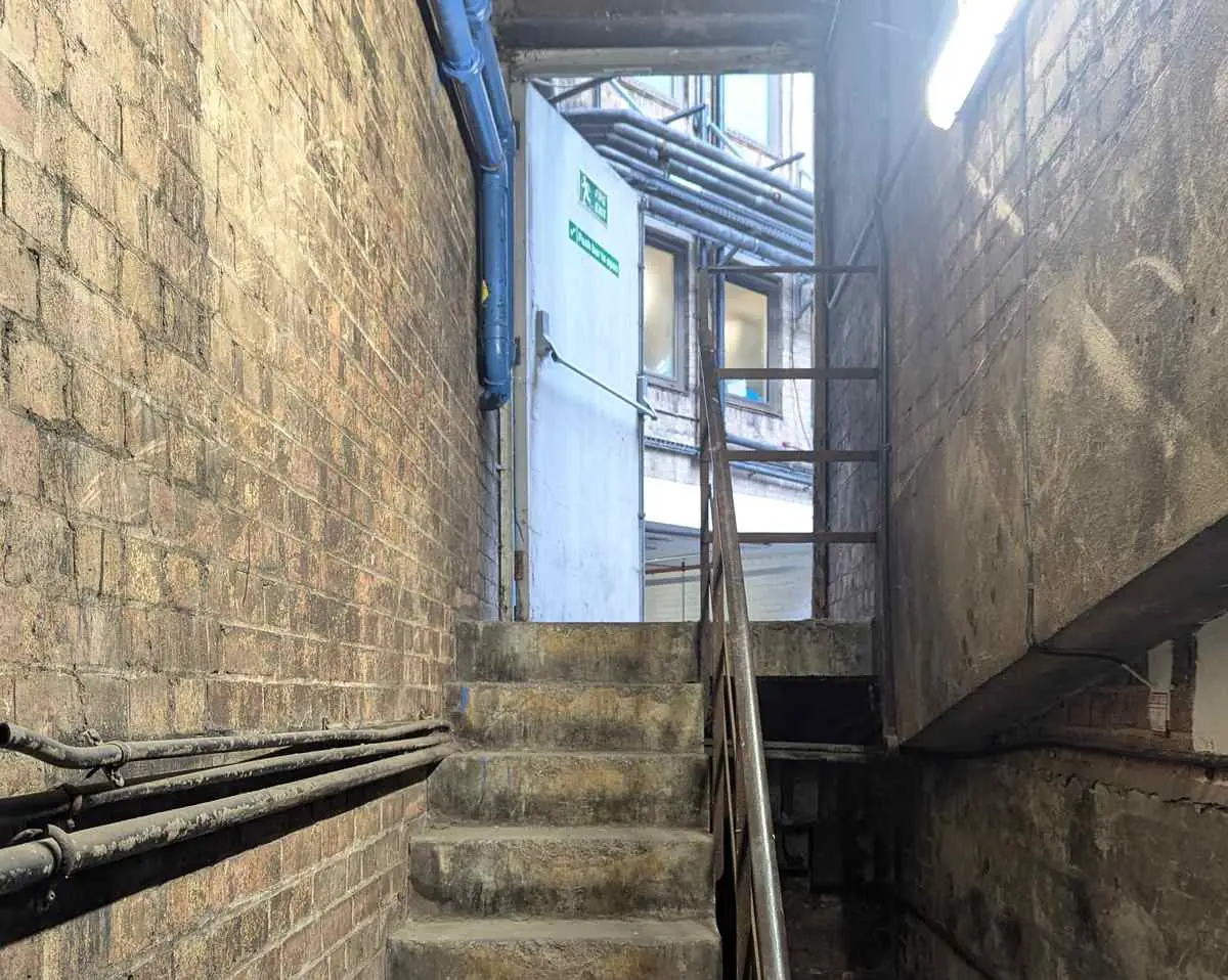 Narrow brick escape stair with worn steps and surface-mounted pipework.